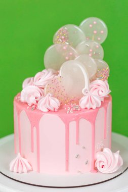 Çikolata parçalı, kremalı pembe kremalı kek. Üzerinde krema ve izomalt lolipoplar var. Yeşil arka planda nefis bir doğum günü pastası. Bir menü veya şekerleme kataloğu için resim. 