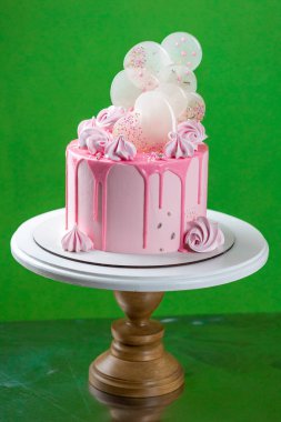 Çikolata parçalı, kremalı pembe kremalı kek. Üzerinde krema ve izomalt lolipoplar var. Yeşil arka planda nefis bir doğum günü pastası. Bir menü veya şekerleme kataloğu için resim. 