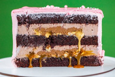 Çikolata parçalı dilimlenmiş pembe krem peynirli pasta. Krema ve izomalt lolipoplarla süslenmiş. Yeşil arka planda nefis bir doğum günü pastası. Bir menü veya şekerleme kataloğu için resim. 