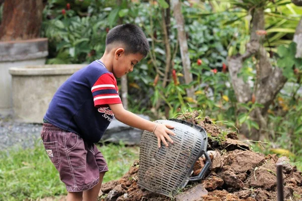 Asian boy pours soil from a bucket