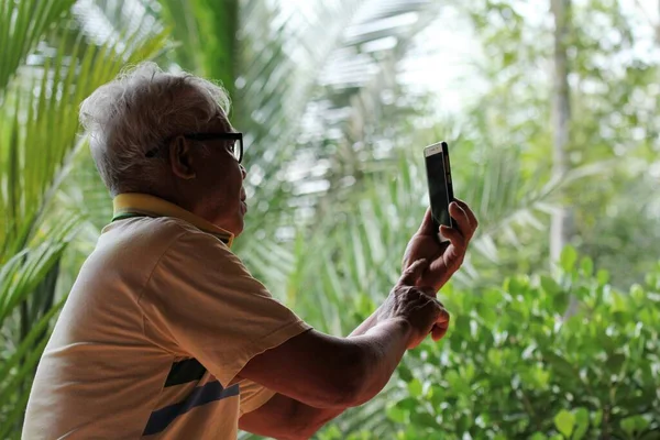 Old Asian man taking pictures with a mobile phone