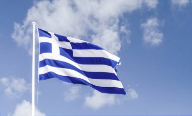Mavi gökyüzüne karşı rüzgarda dalgalanan Yunan bayrağı.