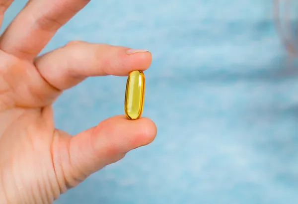 Close-up of fingers holding a fish oil capsule. — Stock Photo, Image
