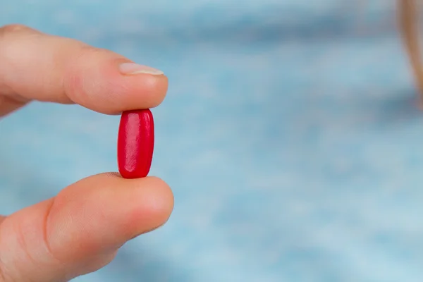 Gros plan des doigts tenant une pilule rouge . Photo De Stock