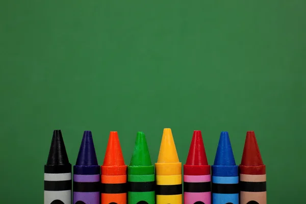 Crayon tops with a green chalkboard background — Stock Photo, Image