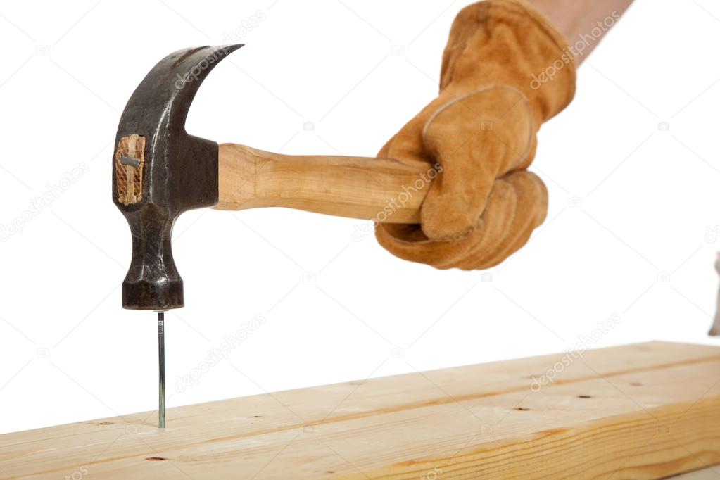 A gloved hand hammering a nail in a piece of wood