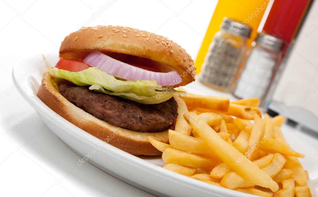 Hamburger and fries with ketchup and mustard, salt and pepper at a