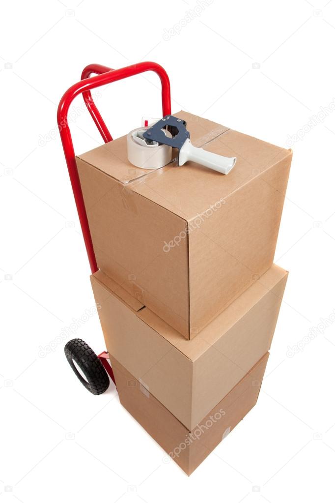 A red hand truck on white with boxes and a tape gun