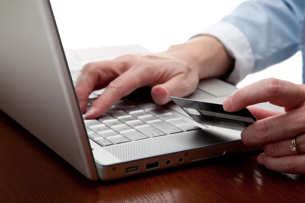 Mão segurando um cartão de crédito sobre um computador — Fotografia de Stock