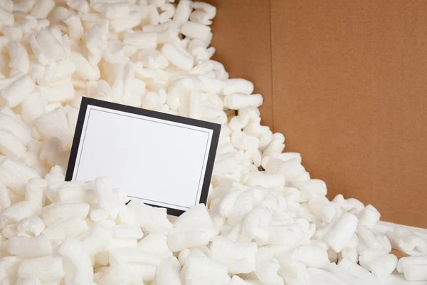 Notecard in packing peanuts with cardboard background — Stock Photo, Image