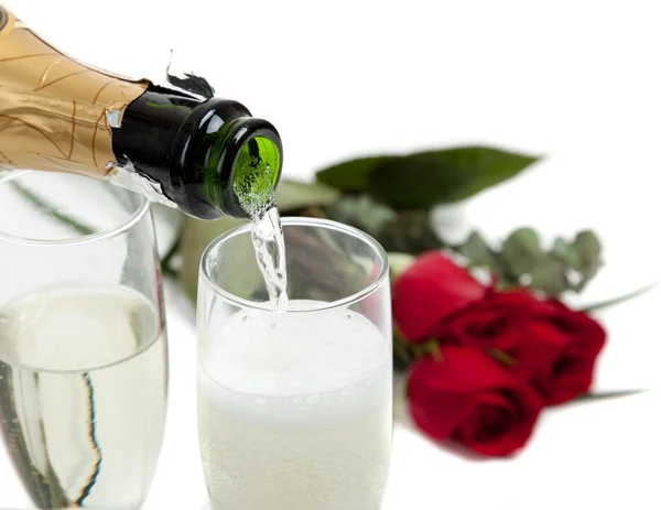 Champagne poring into glasses with roses in the background — Stock Photo, Image