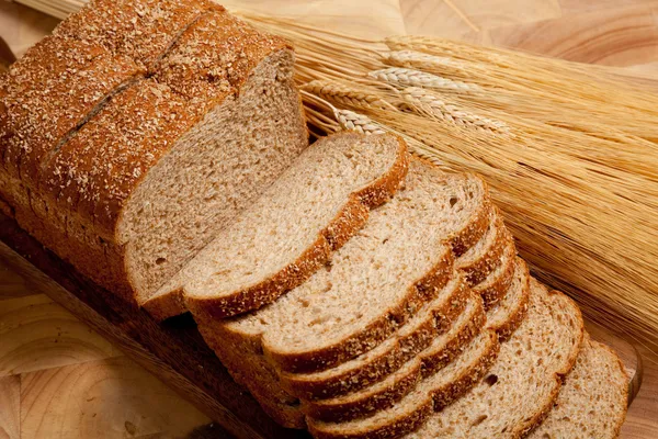 A loaf of bread with a shock of wheat on a wooden board — Stock Photo, Image