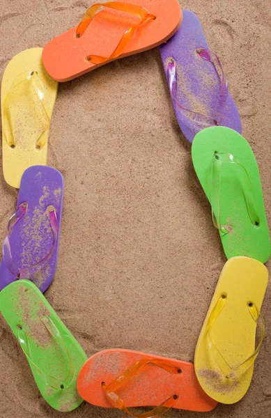 Bordüre aus verschiedenfarbigen Flipflops auf Sand — Stockfoto