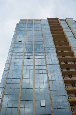 Aynalı panoramik camlı çok katlı bina, gökyüzünün arka planına karşı perspektif olarak aşağıdan çekilir