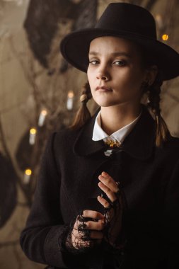 Cadılar Bayramı için siyahlı genç cadı portresi. Arka planda kuru dallar, örümcek ağları ve eski kaledeki mumlar.