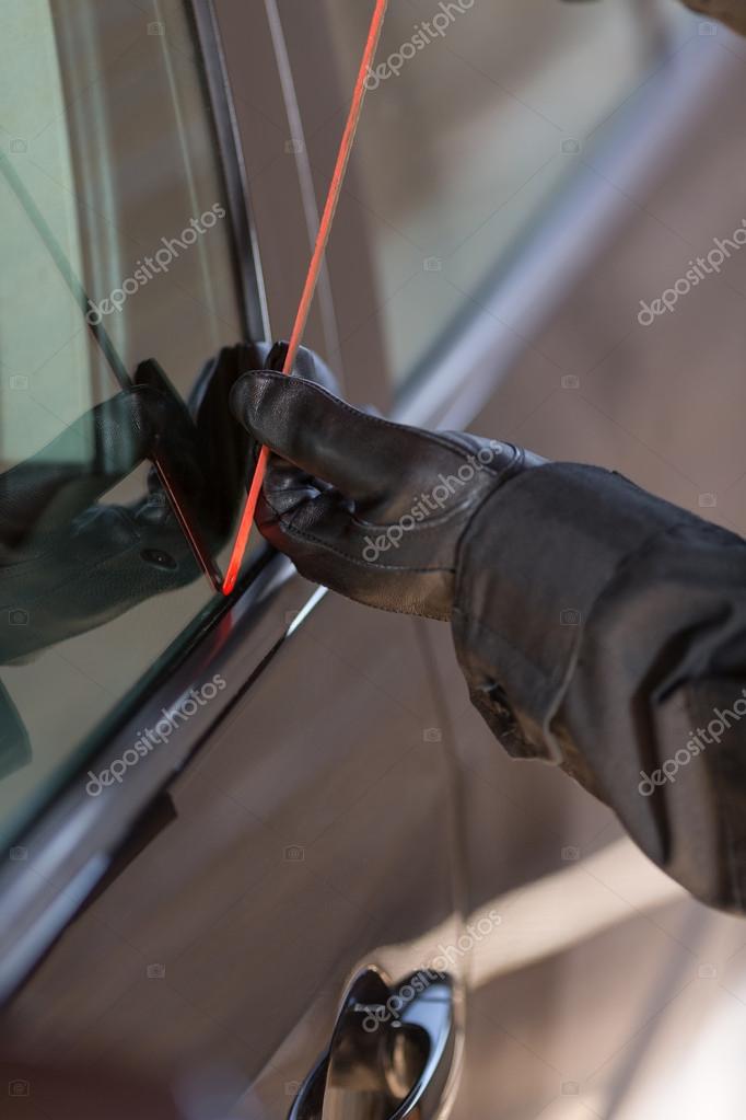 Thief picking the lock of a car parked on the street