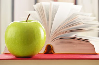 Composition with green apple and books on the table