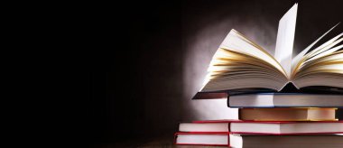 Bir yığın kitabın üzerinde açık bir kitap bulunan kompozisyon. 
