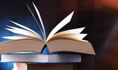 Bir yığın kitabın üzerinde açık bir kitap bulunan kompozisyon. 