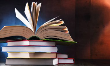 Bir yığın kitabın üzerinde açık bir kitap bulunan kompozisyon. 