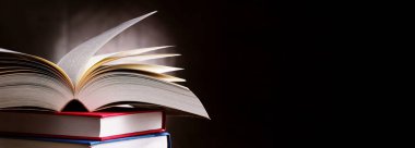 Bir yığın kitabın üzerinde açık bir kitap bulunan kompozisyon. 