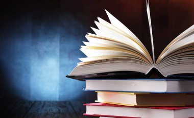 Bir yığın kitabın üzerinde açık bir kitap bulunan kompozisyon. 