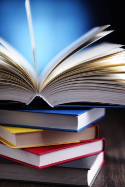 Bir yığın kitabın üzerinde açık bir kitap bulunan kompozisyon. 