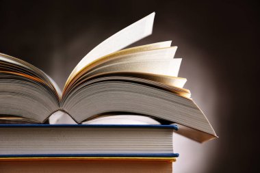 Bir yığın kitabın üzerinde açık bir kitap bulunan kompozisyon. 