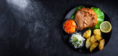 Patates ve sebze salatalı ekmek kırıntılarıyla kaplı domuz pirzolası.