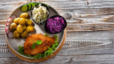 Patates ve sebze salatalı ekmek kırıntılarıyla kaplı domuz pirzolası.