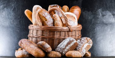 Hasır sepet içinde çeşitli fırın ürünleri ve ekmek ve rulo ekmekler var.