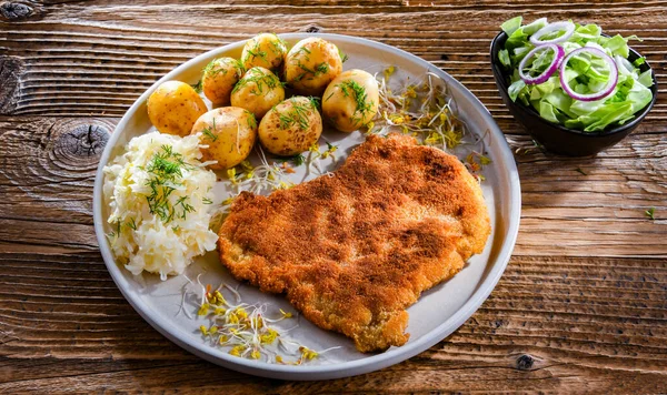 Pork breaded cutlet coated with breadcrumbs served with potatoes and cabbage