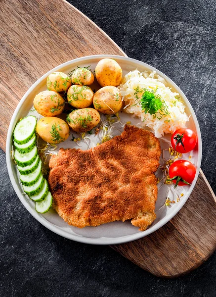 Pork breaded cutlet coated with breadcrumbs served with potatoes and cabbage