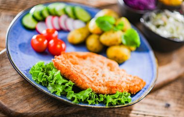 Patates ve sebze salatalı ekmek kırıntılarıyla kaplı domuz pirzolası.