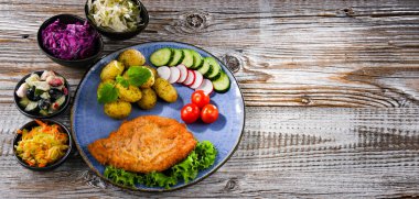 Patates ve sebze salatalı ekmek kırıntılarıyla kaplı domuz pirzolası.