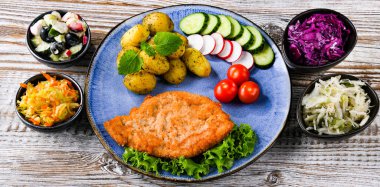 Patates ve sebze salatalı ekmek kırıntılarıyla kaplı domuz pirzolası.