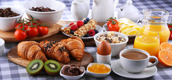 Breakfast served with coffee, orange juice, croissants, pancake, egg, cereals and fruits.