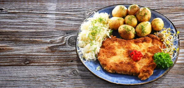 Pork breaded cutlet coated with breadcrumbs served with potatoes and cabbage