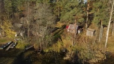Göl kıyısındaki sonbahar ormanında rahat ahşap bir evin havadan görünüşü. Tekneler ve evin yakınında bir rıhtım. Aile tatili kavramı.