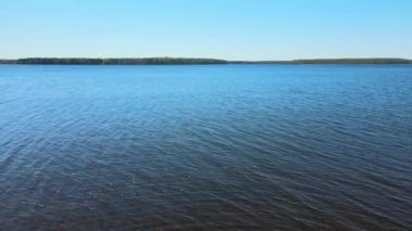 Rusya, Moskova bölgesi, Puşkino, Uchinskoe rezervuarı (Akulovskoe rezervuarı). Güneşli bir havada suyun mavi genişliğinde uçan bir uçağın havadan videosu. Orman uzakta, küçük dalgalar.