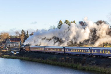 Rusya, Karelia, Sortavala, 08.09.2021. Sortavala istikametindeki Ruskeala Ekspresi adlı Retro treni - Ruskeala Dağı Parkı, göl kenarındaki demiryolu üzerinde ve bacadan dumanlar çıkıyor..