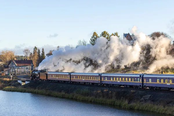 Rusya, Karelia, Sortavala, 08.09.2021. Sortavala istikametindeki Ruskeala Ekspresi adlı Retro treni - Ruskeala Dağı Parkı, göl kenarındaki demiryolu üzerinde ve bacadan dumanlar çıkıyor..