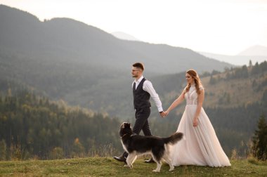 Gün batımında dağlarda köpek gezdiren bir çift. Dağlarda romantik bir akşam.