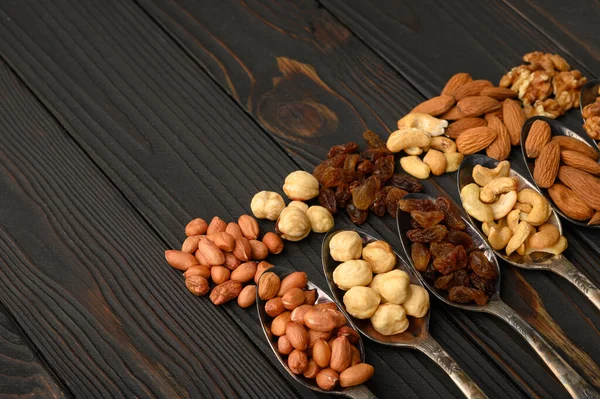 Hazelnut, cashews, raisins, almonds, peanuts, walnuts in silver spoons on a rustic background