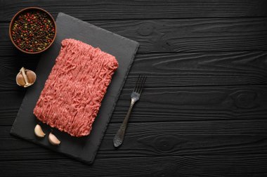 Tahta kesme tahtasındaki taze çiğ et ya da tavuk eti kekik, baharat ve sarımsaklı. Siyah ahşap arka plan. Üst Manzara. Boşluğu kopyala.