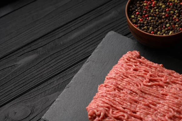 Mix of different types of pepper and minced meat on a black rustic background. Place for a logo.
