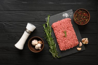 Tahta kesme tahtasındaki taze çiğ et ya da tavuk eti kekik, baharat ve sarımsaklı. Siyah ahşap arka plan. Üst Manzara. Boşluğu kopyala.