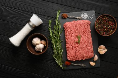 Tahta kesme tahtasındaki taze çiğ et ya da tavuk eti kekik, baharat ve sarımsaklı. Siyah ahşap arka plan. Üst Manzara. Boşluğu kopyala.