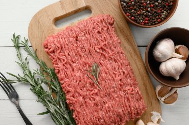 Tahta kesme tahtasındaki taze çiğ et ya da tavuk eti kekik, baharat ve sarımsaklı. Beyaz ahşap arka plan. Üst Manzara. Boşluğu kopyala.