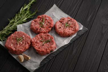 Kasap tahtasına çiğ sığır burger köftesi, biberiye ve biber. Siyah arka plan. Yukarıdan görüntüle.